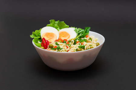Beautiful Noodle Dish with Green Pea, Carrot, Eggs, Red Hot Pepper and Greens on Black Background. Instant Noodles with Vegetablesの写真素材
