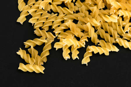 A Heap of Uncooked Fusilli Pasta Scattered on Black Table. Raw and Dry Macaroni. Unhealthy and Fat Food. Italian Cultureの写真素材