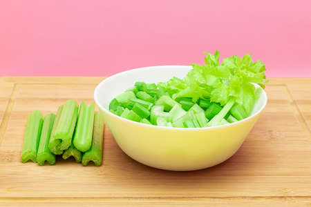 Fresh Chopped Celery Slices in White Bowl with Celery Sticks on Bamboo Cutting Board. Vegan and Vegetarian Culture. Raw Food. Healthy Diet with Negative Calorie Contentの写真素材