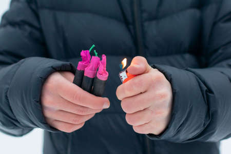 Guy Sets Fire to the Flash Noise Firecrackers Outdoors in Winter at Daytime. Loud and Dangerous New Years Entertainment. Hooliganism with Pyrotechnics. Noise of Petards in Public Placesの写真素材
