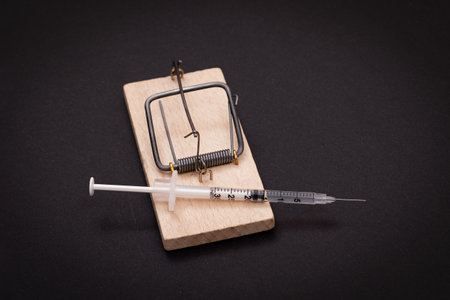 Drug Addict, Heroin Hazard or Dose Trap Concept - Disposable Insulin Syringe with Drug Dose Inside Lying in Wooden Mousetrap on Black Backgroundの写真素材