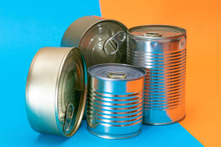 A Group of Stacked Tin Cans with Blank Edges on Split Blue and Orange Background. Canned Food. Different Aluminum Cans for Safe and Long Term Storage of Food. Steel Sealed Food Storage Containersの写真素材