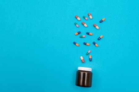 Global Pharmaceutical Industry and Medicinal Products - Colored Pills or Capsules Scattered from the Pill Container, Lying on Blue Backgroundの写真素材