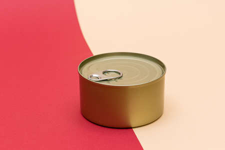 Unopened Tin Can with Blank Edge on Split Red and Beige Background. Canned Food. Aluminum Can for Safe and Long Term Storage of Food. Steel Sealed Food Storage Containerの写真素材