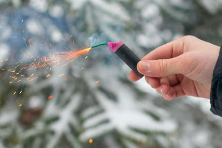 Burning Firecracker in a Hand. Guy Holding a Petard Outdoors in Winter at Daytime. Loud and Dangerous New Years Entertainment. Hooliganism with Pyrotechnics. Noise of Firecrackers in Public Placesの写真素材