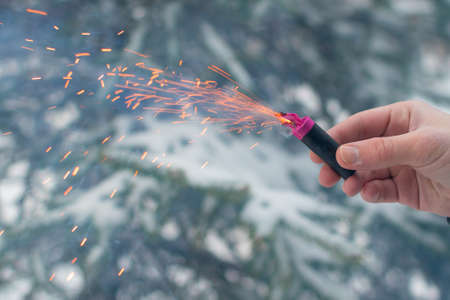 Burning Firecracker in a Hand. Guy Holding a Petard Outdoors in Winter at Daytime. Loud and Dangerous New Years Entertainment. Hooliganism with Pyrotechnics. Noise of Firecrackers in Public Placesの写真素材
