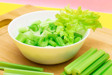Fresh Chopped Celery Slices in White Bowl with Celery Sticks on Bamboo Cutting Board. Vegan and Vegetarian Culture. Raw Food. Healthy Diet with Negative Calorie Contentの写真素材