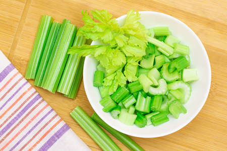 Fresh Chopped Celery Slices in White Bowl with Celery Sticks on Bamboo Cutting Board. Vegan and Vegetarian Culture. Raw Food. Healthy Diet with Negative Calorie Contentの写真素材