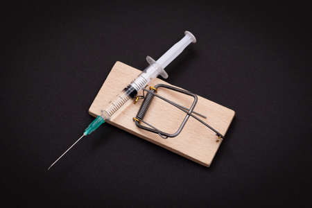 Drug Addict, Heroin Hazard or Dose Trap Concept - Disposable Syringe with Drug Dose Inside Lying in Wooden Mousetrap on Black Backgroundの写真素材