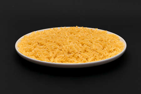 Uncooked Fusilli Pasta Lying on White Plate on Black Background. Raw and Dry Macaroni. Unhealthy and Fat Foodの写真素材