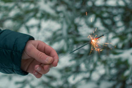 Burning Sparklers in a Hand Outdoors in Winter in Evening. New Year Celebration Partyの写真素材