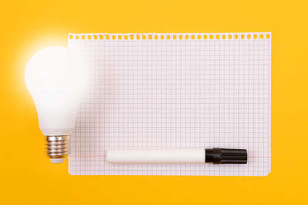 A Power Saving Lamp with Notepad Lying on Yellow Table, Blank Template with Copy Space - Top View, Flat Layの写真素材
