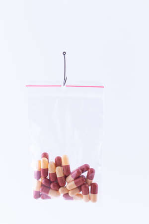The Pharmaceutical Trap and Drug Addiction - Colored Pills or Tablets Hanging in Small lock Bag on a Fishing Hook Against the White Backgroundの写真素材