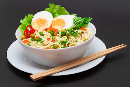 Beautiful Noodle Dish with Green Pea, Carrot, Eggs, Red Hot Pepper and Greens on Black Background. Instant Noodles with Vegetablesの写真素材