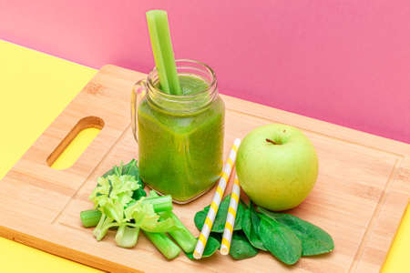 Fresh Green Smoothie of Apple, Celery, and Spinach in Glass Smoothie Jar with Yellow Cocktail Straw on Wooden Cutting Board. Vegan Detox Drink. Vegetarian Culture. Healthy Eating and Fruit Dietの写真素材