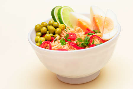 Beautiful Noodle Dish with Green Pea, Eggs, Red Hot Pepper, Greens and Lime on White Background. Instant Noodlesの写真素材