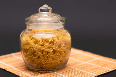 Uncooked Fusilli Pasta in Glass Jar on Black Background. Raw and Dry Macaroni. Unhealthy and Fat Food. Italian Cultureの写真素材