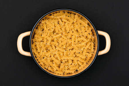 Uncooked Fusilli Pasta in Metal Pot on Black Background. Raw and Dry Macaroni. Unhealthy and Fat Food. Italian Cultureの写真素材