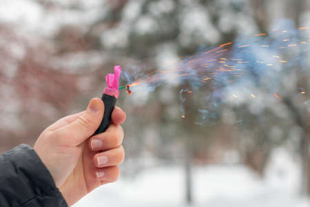 Burning Firecracker in a Hand. Guy Holding a Petard Outdoors in Winter at Daytime. Loud and Dangerous New Years Entertainment. Hooliganism with Pyrotechnics. Noise of Firecrackers in Public Placesの写真素材