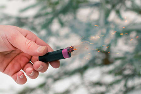 Burning Firecracker in a Hand. Guy Holding a Petard Outdoors in Winter at Daytime. Loud and Dangerous New Years Entertainment. Hooliganism with Pyrotechnics. Noise of Firecrackers in Public Placesの写真素材