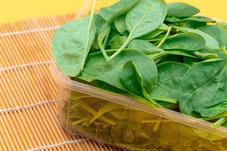 Fresh Baby Spinach Leaves in Transparent Plastic Package on Wooden Mat. Vegan and Vegetarian Culture. Raw Food, Green Leaves. Healthy Dietの写真素材