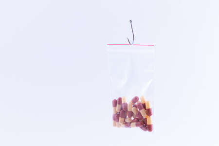 The Pharmaceutical Trap and Drug Addiction - Colored Pills or Tablets Hanging in Small Ziplock Bag on a Fishing Hook Against the White Backgroundの写真素材