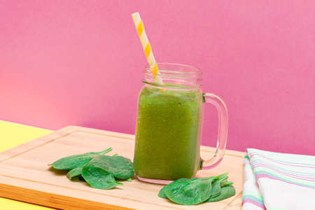 Fresh Green Smoothie of Apple, Celery, and Spinach in Glass Smoothie Jar with Yellow Cocktail Straw on Wooden Cutting Board. Vegan Detox Drink. Vegetarian Culture. Healthy Eating and Fruit Dietの写真素材
