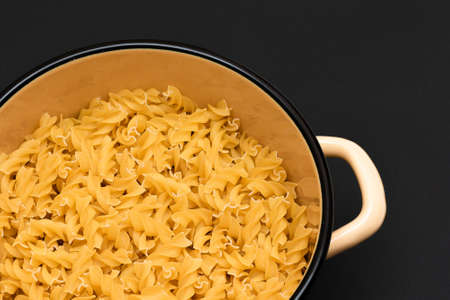 Uncooked Fusilli Pasta in Metal Pot on Black Background. Raw and Dry Macaroni. Unhealthy and Fat Food. Italian Cultureの写真素材
