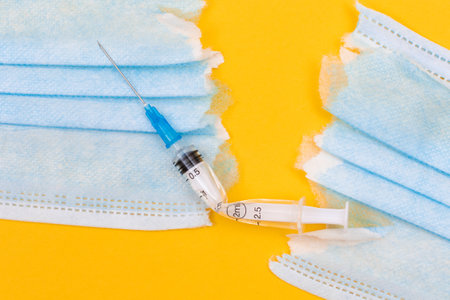 Anti Vaccine Movement and Anti Mask Concept - Broken Medical Syringe and Torn Medical Face Mask Lying on Yellow Background. Pandemic and Lockdown End - Top View, Flat Layの写真素材