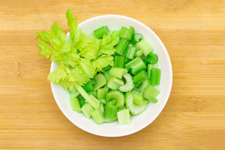 Fresh Chopped Celery Slices in White Bowl on Bamboo Cutting Board - Top View. Vegan and Vegetarian Culture. Raw Food. Healthy Diet with Negative Calorie Contentの写真素材