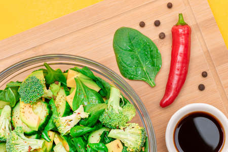 Fresh Green Salad of Avocado, Broccoli, Spinach and Cucumber with Soy Sauce and Red Hot Pepper on Wooden Cutting Board. Vegan Salad. Vegetarian Culture. Raw Food. Healthy Eating and Vegetable Dietの写真素材