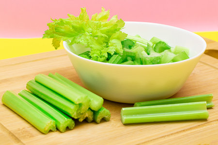 Fresh Chopped Celery Slices in White Bowl with Celery Sticks on Bamboo Cutting Board. Vegan and Vegetarian Culture. Raw Food. Healthy Diet with Negative Calorie Contentの写真素材