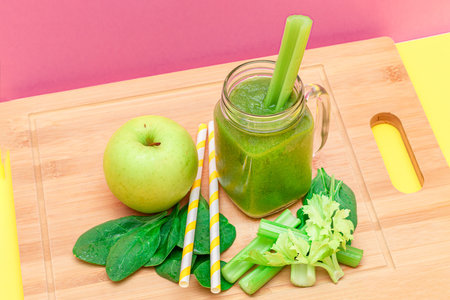 Fresh Green Smoothie of Apple, Celery, and Spinach in Glass Smoothie Jar with Yellow Cocktail Straw on Wooden Cutting Board. Vegan Detox Drink. Vegetarian Culture. Healthy Eating and Fruit Dietの写真素材