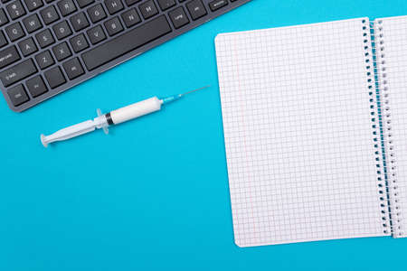 Vaccination, Immunology or Revaccination Concept - A Medical Syringe Lying on Blue Table in Doctors Office in a Hospital or Clinic. Opened Blank Notepad - Mock Up with Copy Spaceの写真素材