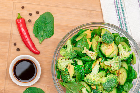 Fresh Green Salad of Avocado, Broccoli, Spinach and Cucumber with Soy Sauce and Red Hot Pepper on Wooden Cutting Board. Vegan Salad. Vegetarian Culture. Raw Food. Healthy Eating and Vegetable Dietの写真素材