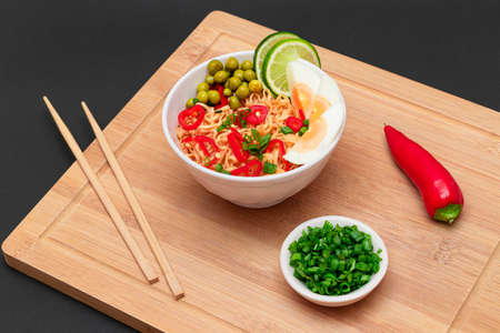 Beautiful Noodle Dish with Green Pea, Eggs, Red Hot Pepper, Greens and Lime with Chopsticks on Bamboo Cutting Board. Instant Noodlesの写真素材
