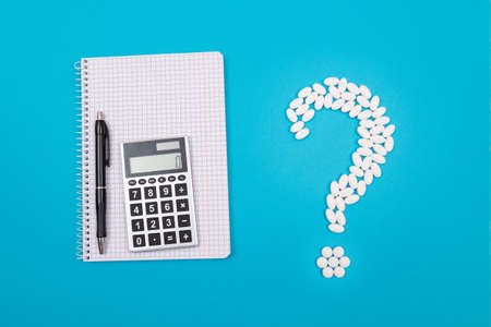 Treatment Costs and Budget. Question Mark Made from White Pills and Tablets with Calculator and Notepad, Lying on Blue Background. Global Pharmaceutical Industry and Medicinal Productsの写真素材