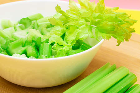 Fresh Chopped Celery Slices in White Bowl with Celery Sticks on Bamboo Cutting Board. Vegan and Vegetarian Culture. Raw Food. Healthy Diet with Negative Calorie Contentの写真素材