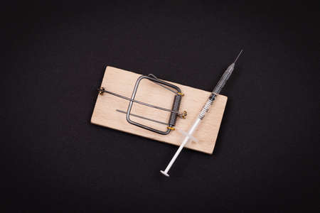 Drug Addict, Heroin Hazard or Dose Trap Concept - Disposable Insulin Syringe with Drug Dose Inside Lying in Wooden Mousetrap on Black Backgroundの写真素材