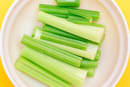 Fresh Chopped Celery Sticks with Water Drops in White Bowl - Top View. Vegan and Vegetarian Culture. Raw Food. Healthy Diet with Negative Calorie Contentの写真素材