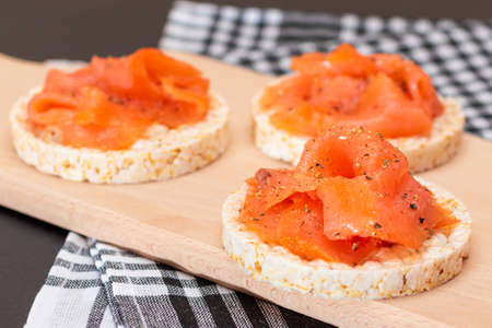 Tasty Rice Cake Sandwiches with Fresh Salmon Slices on Wooden Cutting Board. Easy Breakfast and Diet Food. Crispbread with Red Fish. Healthy Dietary Snackの写真素材