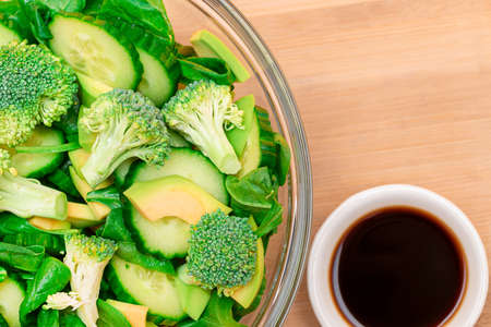 Fresh Green Salad of Avocado, Broccoli, Spinach and Cucumber for Detox with Soy Sauce on Wooden Cutting Board. Vegan Salad. Vegetarian Culture. Raw Food. Healthy Eating and Vegetable Dietの写真素材