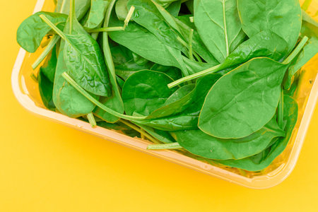 Fresh Baby Spinach Leaves in Transparent Plastic Package on Yellow Background - Top View. Vegan and Vegetarian Culture. Raw Food, Green Leaves. Healthy Dietの写真素材