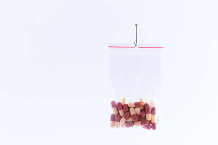 The Pharmaceutical Trap and Drug Addiction - Colored Pills or Tablets Hanging in Small Ziplock Bag on a Fishing Hook Against the White Backgroundの写真素材