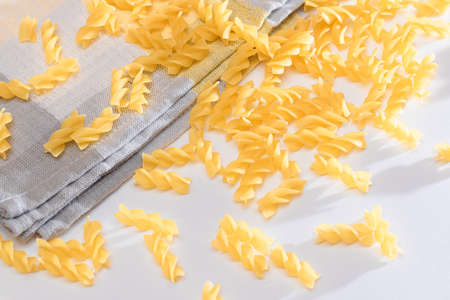 Uncooked Fusilli Pasta Scattered on White Table. Raw and Dry Macaroni. Fat and Unhealthy Foodの写真素材