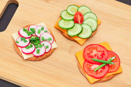 Different Cracker Sandwiches with Tomato, Cucumber, Radish and Cheese on Cutting Board. Easy Breakfast. Diet Food. Quick and Healthy Sandwiches. Crispbread with Tasty Filling. Healthy Dietary Snackの写真素材
