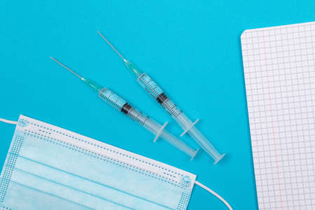 Vaccination, Immunology or Revaccination Concept - Two Medical Syringe Lying on Blue Table in Doctors Office in a Hospital or Clinic. Opened Blank Notepad - Mock Up with Copy Spaceの写真素材