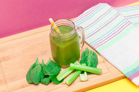 Fresh Green Smoothie of Apple, Celery, and Spinach in Glass Smoothie Jar with Yellow Cocktail Straw on Wooden Cutting Board. Vegan Detox Drink. Vegetarian Culture. Healthy Eating and Fruit Dietの写真素材