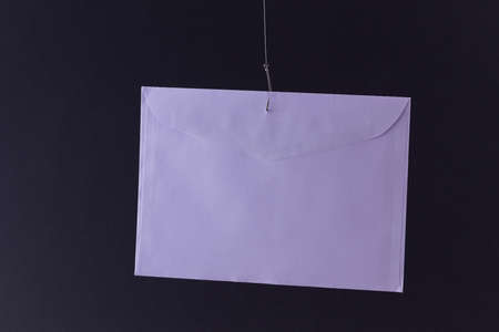 Violet Envelope Hanging on a Fishing Hook Against the Black Backgroundの写真素材