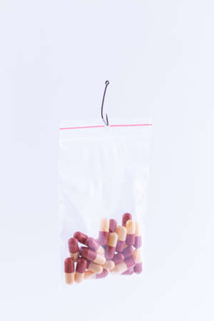 The Pharmaceutical Trap and Drug Addiction - Colored Pills or Tablets Hanging in Small Ziplock Bag on a Fishing Hook Against the White Backgroundの写真素材